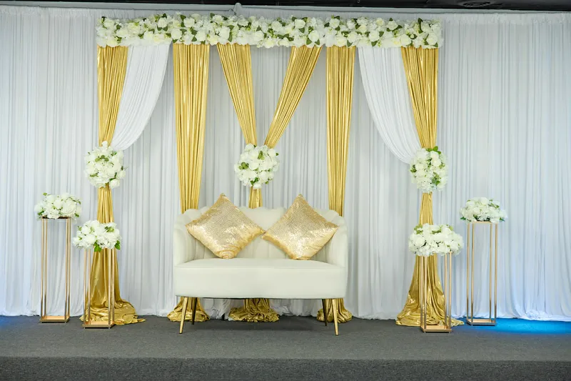 Gold and white draped backdrop with loveseat and white floral arrangements at MP Venue
