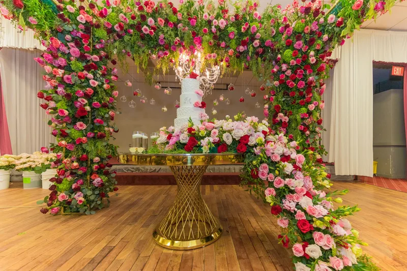 Wedding cake on gold table under floral arch with roses and chandelier at MP Venue Event Center in DFW
