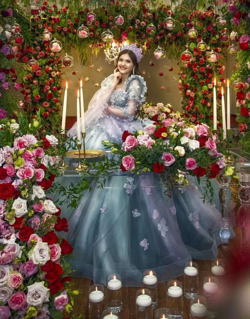 Quinceañera in blue gown under pink and red floral arch